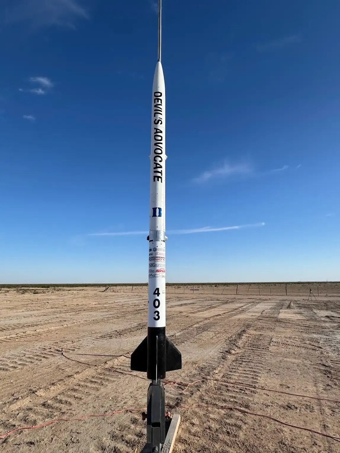 The team's rocket, Devil's Advocate, standing on its launch rail in the desert under a clear sky.