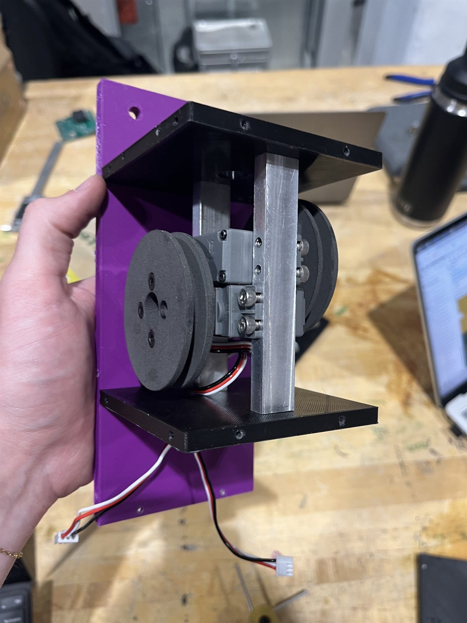 The guided recovery mechanism held in one hand: machined aluminum cross strut, black printed side plates, servo and pulleys mounted on a purple printed base plate.